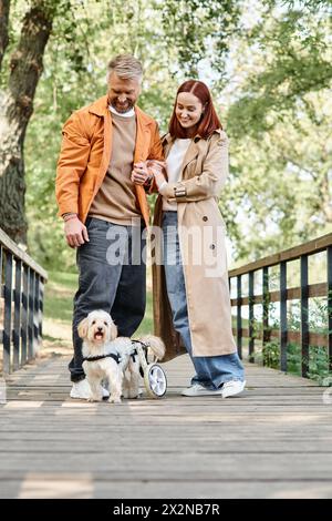 Una coppia adulta in un abbigliamento casual cammina il proprio cane su un ponte in un parco. Foto Stock