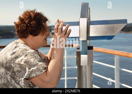 una donna anziana guarda attraverso il telescopio il paesaggio a bordo della nave Foto Stock