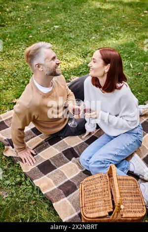 Coppia che si gode un picnic, tenendo i bicchieri da vino su una coperta. Foto Stock