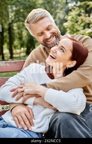 Un uomo e una donna in un abbigliamento casual seduti tranquillamente su una panchina in un parco. Foto Stock