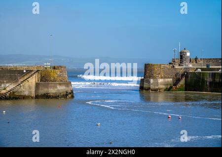 Una vista delle onde che si infrangono attraverso l'entrata del porto con la bassa marea a Saundersfoot, Galles, in una luminosa giornata primaverile Foto Stock