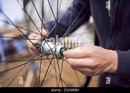 Uomo irriconoscibile che monta un assale ruota per bici dopo averlo smontato per la pulizia e l'ingrassaggio nell'ambito di un servizio di manutenzione per biciclette. Persone vere Foto Stock