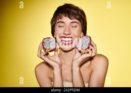 Una donna tiene giocosamente due frutti di drago davanti al suo viso. Foto Stock