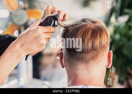 Il giovane parrucchiere vietnamita fa il taglio di capelli al maschio. Vista posteriore. Competenze professionali. Foto Stock