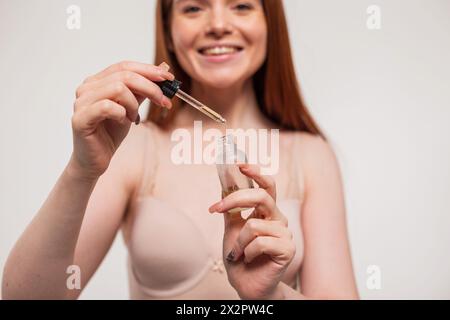 La bellissima ragazza dalla testa rossa felice con Un sorriso carino regge Una goccia di olio cosmetico per idratare la pelle. Bellezza e cura della pelle Foto Stock