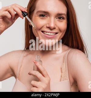 La bellissima ragazza dalla testa rossa fresca con Un sorriso naturale tiene l'olio cosmetico in Un contagocce. Bellezza e cura della pelle Foto Stock