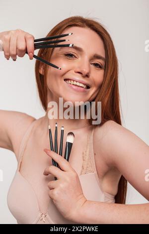 Felice, bella giovane rossa donna con Un sorriso carino tiene in mano Una spazzola per il trucco nello Studio. Bellezza e cura della pelle Foto Stock