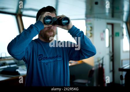 Capitano sul ponte capitano sul ponte della nave portacontainer MS Flintercape, utilizzando un binocolo, durante un viaggio dal porto di Rotterdam verso Sundsvall, Svezia. MRYES Rotterdam NLD - Sundsvall se Containervessel MS Flintercape Noordzee, Baltische Zee, Golf va Paesi Bassi Copyright: XGuidoxKoppesxPhotox Foto Stock