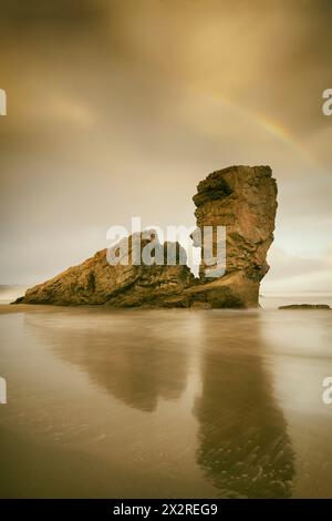 Alba sulla riva con rocce illuminate e arcobaleno, PlayOn de Bayas-Asturias, Spagna Foto Stock