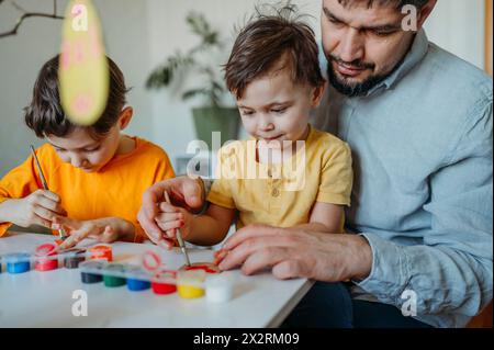Padre con bambini che dipingono uova di Pasqua in cartone Foto Stock