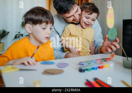 Padre felice con bambini che dipingono uova di Pasqua in cartone a casa Foto Stock