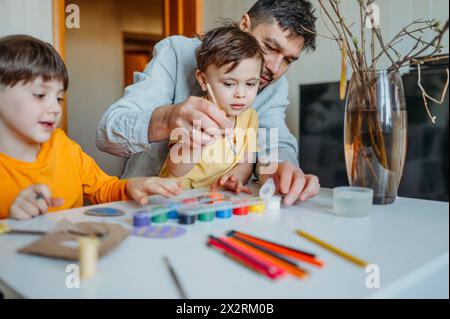 Padre con bambini che dipingono uova di Pasqua in cartone a tavola Foto Stock