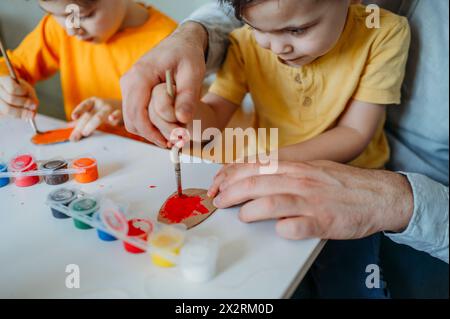 Padre e bambini dipingono uova di Pasqua in cartone a casa Foto Stock
