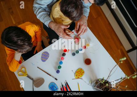 Padre con ragazzi che dipingono uova di Pasqua in cartone a casa Foto Stock