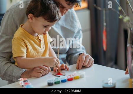 Padre che insegna al figlio a dipingere le uova di Pasqua in cartone con acquerelli Foto Stock