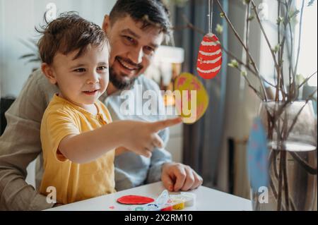 Padre felice con figlio che tocca le uova di Pasqua in cartone sui ramoscelli Foto Stock