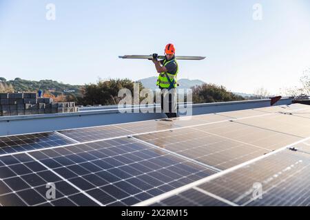 Tecnico solare che trasporta apparecchiature tramite pannelli sul tetto Foto Stock