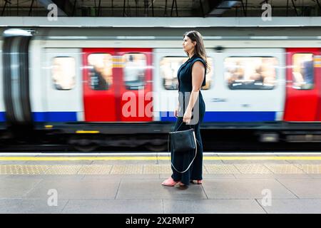 Donna che tiene la borsa e si trova vicino al treno della metropolitana in movimento Foto Stock
