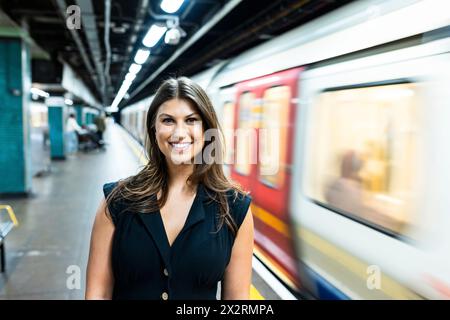 Giovane donna sorridente in piedi vicino al treno della metropolitana in movimento Foto Stock