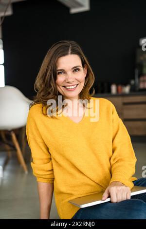 Donna d'affari sorridente con un notebook seduto in un ufficio creativo Foto Stock