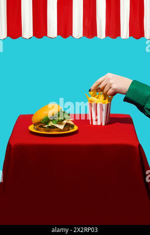 Mano di donna che cerca patatine fritte vicino all'hamburger sul tavolo su sfondo blu Foto Stock