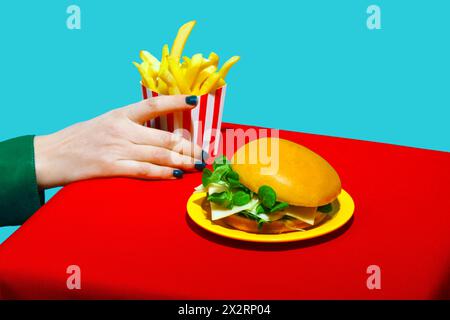 Donna che prende le patatine fritte vicino all'hamburger sul tavolo su sfondo blu Foto Stock