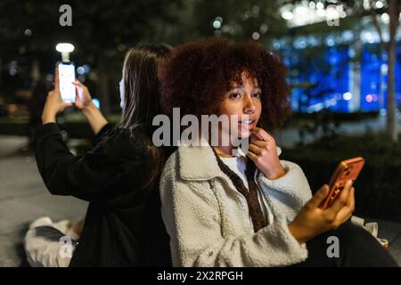 Giovane donna premurosa con un amico che usa lo smartphone di notte Foto Stock