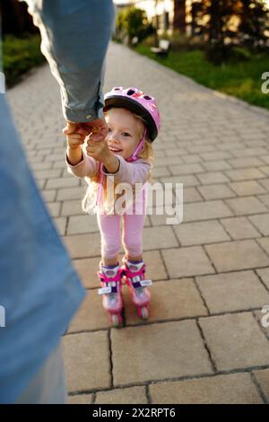 Mano dell'uomo che assiste la figlia a fare pattinaggio a rotelle sul sentiero pedonale Foto Stock