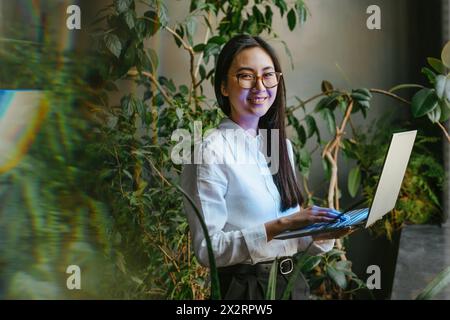 Felice giovane donna d'affari in piedi con il portatile in ufficio Foto Stock