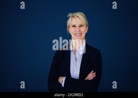 Donna d'affari sorridente in piedi con le braccia incrociate su sfondo blu navy Foto Stock