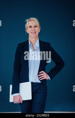 Donna d'affari felice in piedi con un notebook su sfondo blu navy Foto Stock