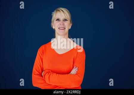 Donna d'affari sorridente in piedi con le braccia incrociate su sfondo blu navy Foto Stock