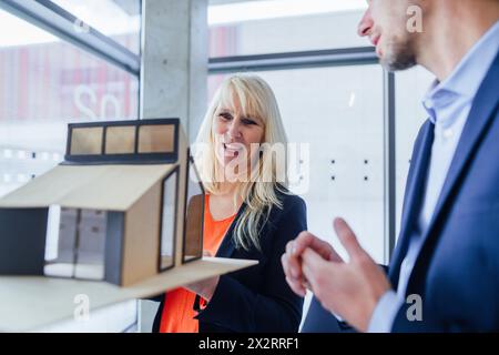 Architetto sorridente che tiene la casa modello e discute con il collega Foto Stock