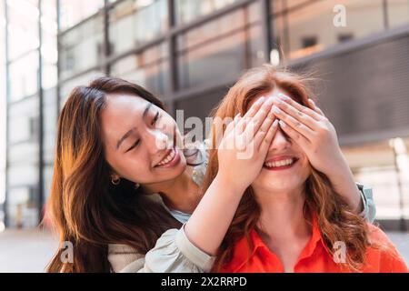 Donna sorridente che copre gli occhi di un amico con le mani Foto Stock