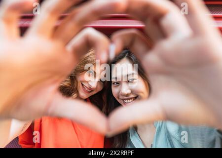 Amici multirazziali sorridenti che danno forma al cuore Foto Stock