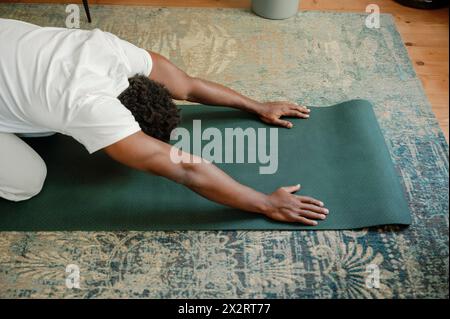 Uomo che si allunga sul tappetino per esercizi facendo yoga a casa Foto Stock