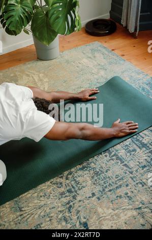 Uomo che si allunga sul tappetino per esercizi facendo yoga a casa al mattino Foto Stock