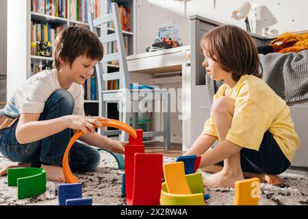 Fratelli che giocano con giocattoli in legno multicolore a casa Foto Stock