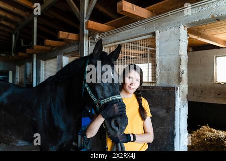 Donna in piedi con cavallo nero in stalla Foto Stock