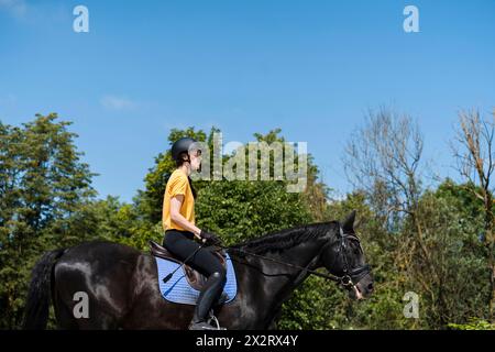 Istruttore che cavalca il cavallo nero al ranch nelle giornate di sole Foto Stock