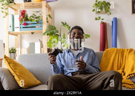 Persona allegra e non binaria che indossa cuffie wireless e gioca ai videogame a casa Foto Stock