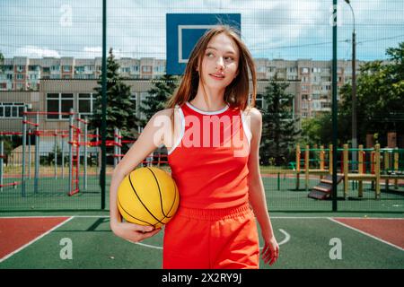 Giocatore di pallacanestro che porta la palla sotto il braccio e cammina nel cortile della scuola Foto Stock