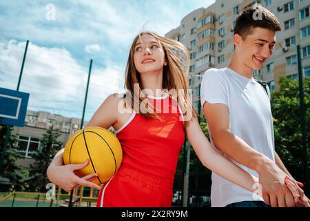 Amici adolescenti sorridenti che si tengono per mano e camminano nel cortile della scuola Foto Stock