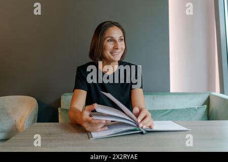 Donna d'affari sorridente seduta con una rivista al bar Foto Stock