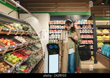 Donna sorridente che cammina con un assistente robot intelligente al negozio di alimentari Foto Stock