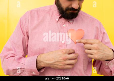 Uomo con cuore rosso su camicia rosa su sfondo giallo Foto Stock