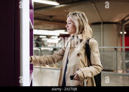 Donna che usa il distributore automatico di biglietti alla stazione ferroviaria Foto Stock