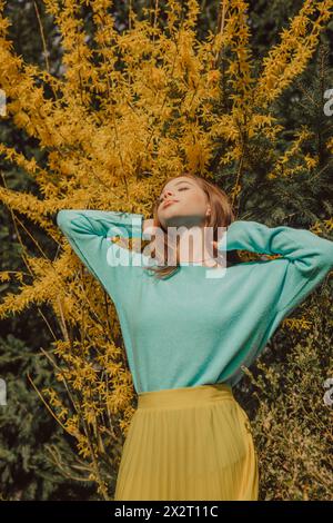 Giovane donna con le mani nei capelli in piedi vicino all'albero fiorito Foto Stock