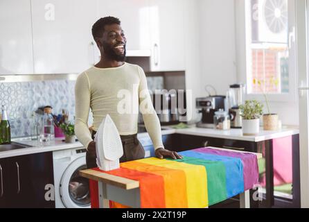 Una persona felice non-binaria che stirava la bandiera arcobaleno a casa Foto Stock