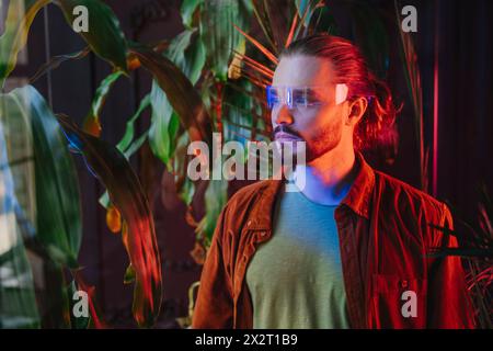 Uomo che indossa occhiali intelligenti e che si trova vicino a piante con luci al neon Foto Stock